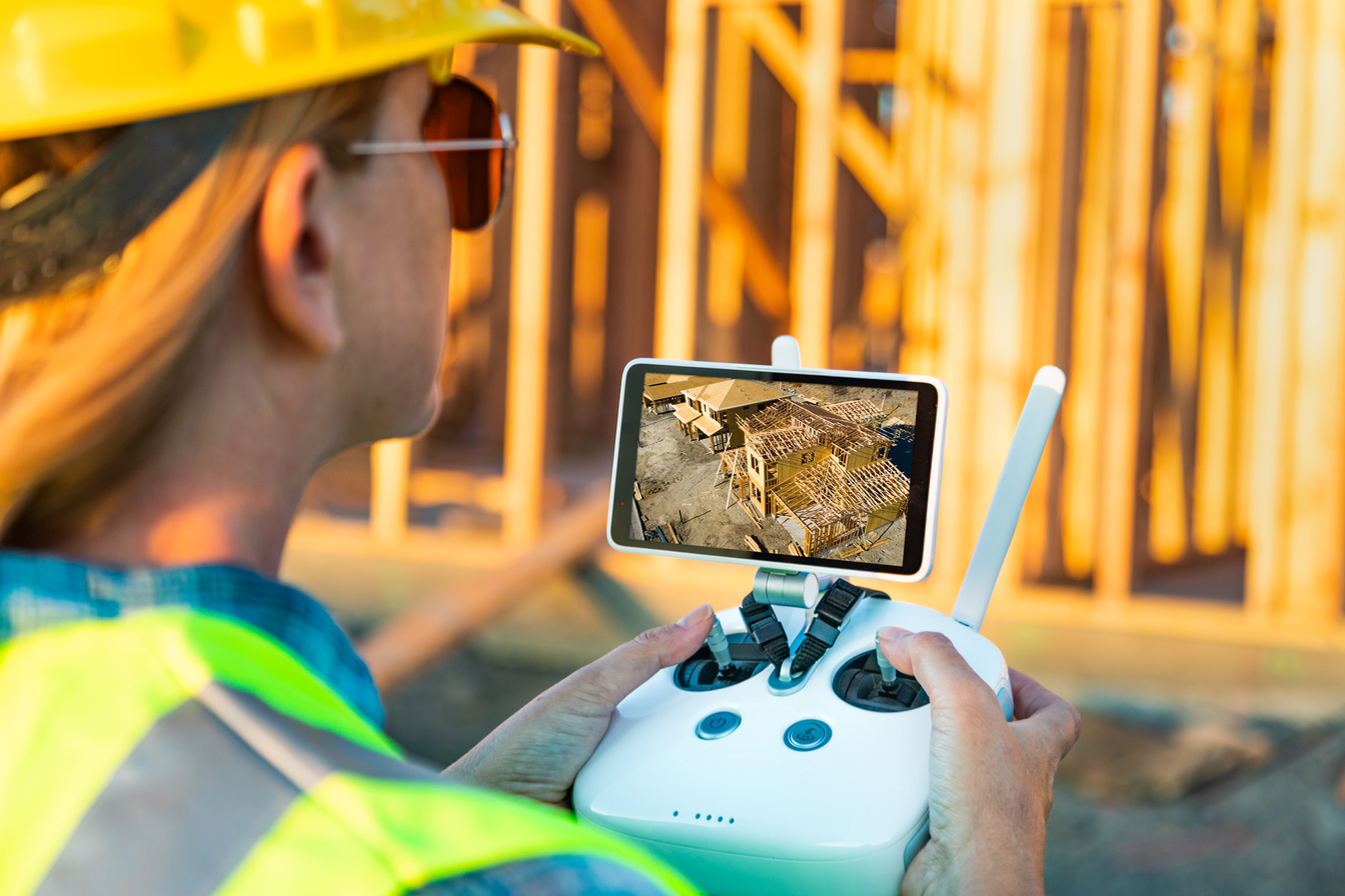 Female Unmanned Aircraft System (UAV) Quadcopter Drone Pilot with Controller Inspecting New House Framing